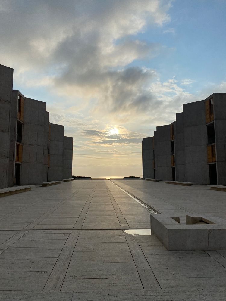 Salk Institute. Two marble and teak buildings frame a marble courtyard with a fountain. The sunset over the Pacific Ocean is in the background.