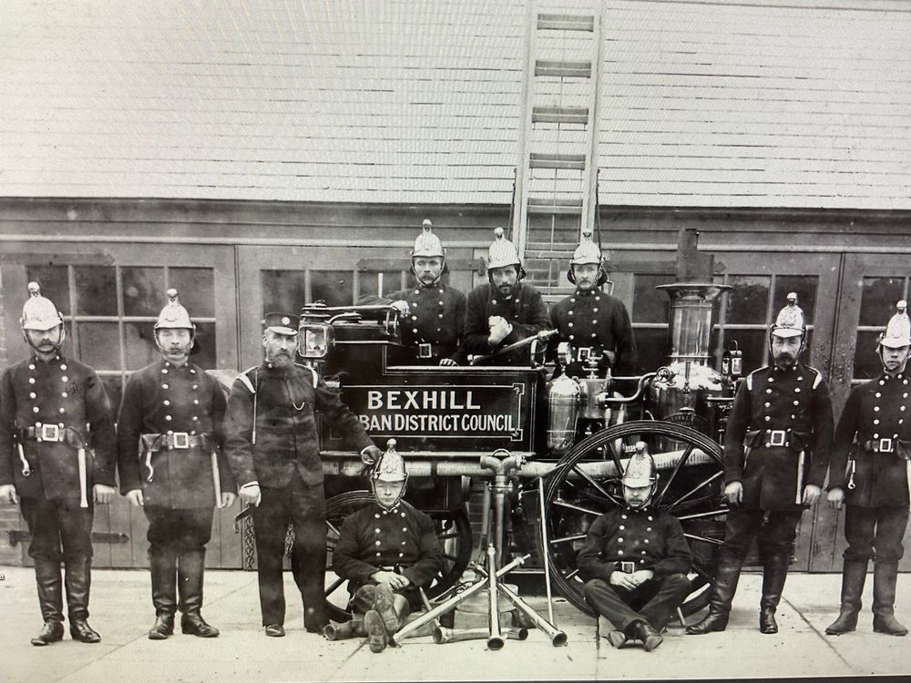 Black and white photograph of the engine shortly after purchase. On the side of it it says Bexhill Urban District Council. There are ten firemen in uniform around the engine. 