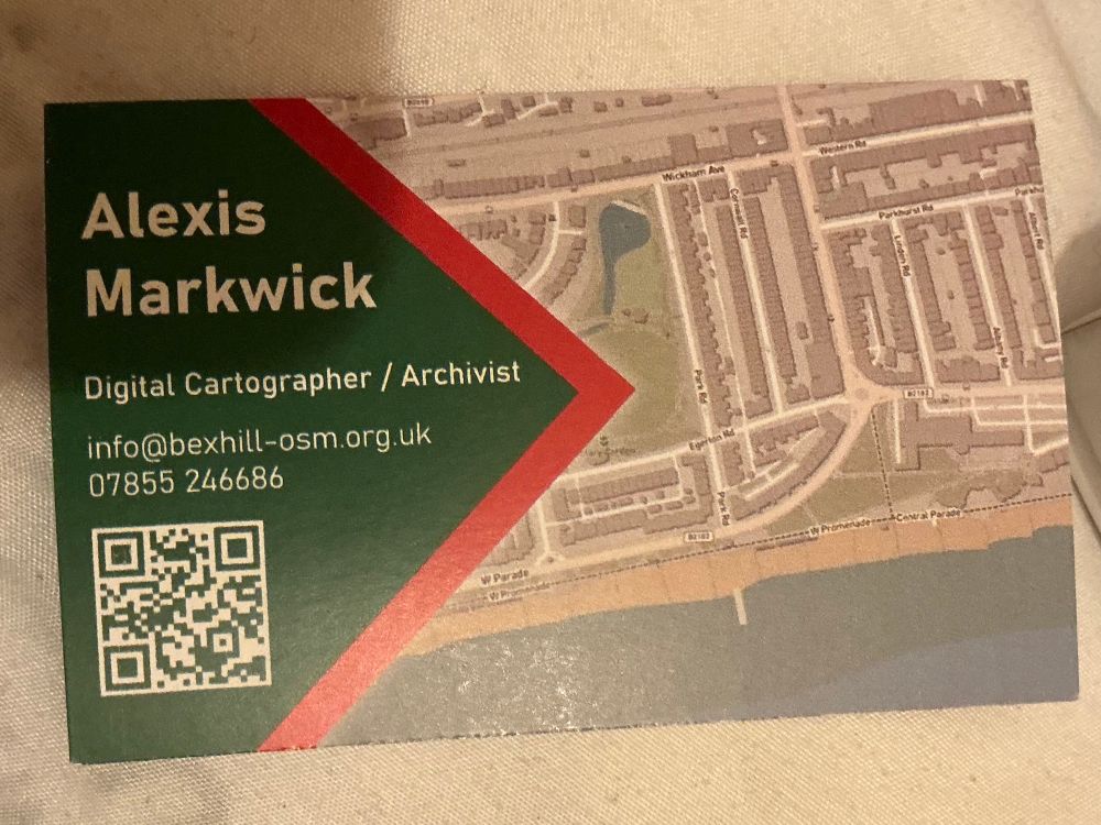 This is the back of the business card. It says Alexis Markwick. Digital Cartographer/Archivist  info@bexhill-osm.org.uk 07855 246686 Then there is a QR code underneath it. To the right is a larger section of map. 