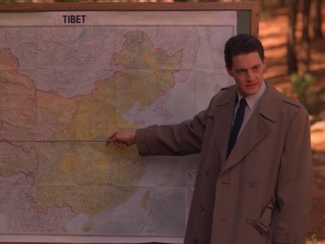 Agent Cooper a character in David Lynch’s Twin Peaks stood in front of a map holding a pointer directed at Tibet. The map is titled “Tibet”.