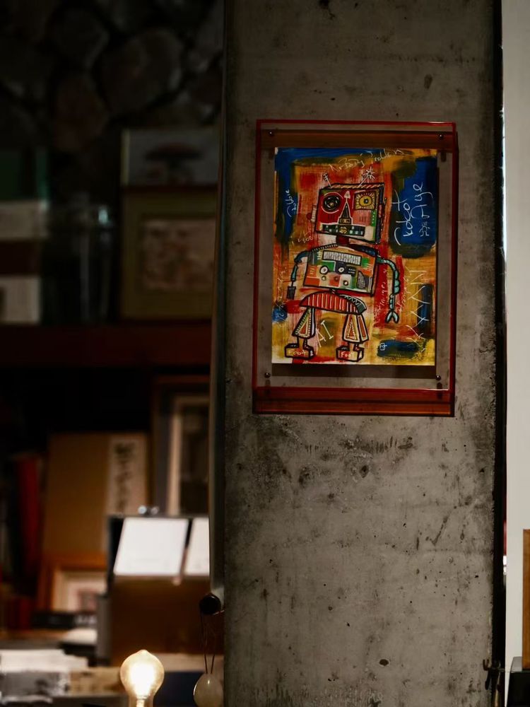 A framed, brightly coloured robot painting hangs on a concrete pillar inside a dimly lit art and antiques gallery in Wenzhou. The artwork stands out against the muted surroundings and is displayed as part of the gallery’s items for sale.