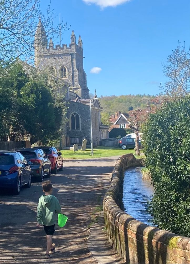 The Misbourne chalk stream retained by an old wall as it passes the church presumably ancient flood protection. Small boy approaching with fishing net.  