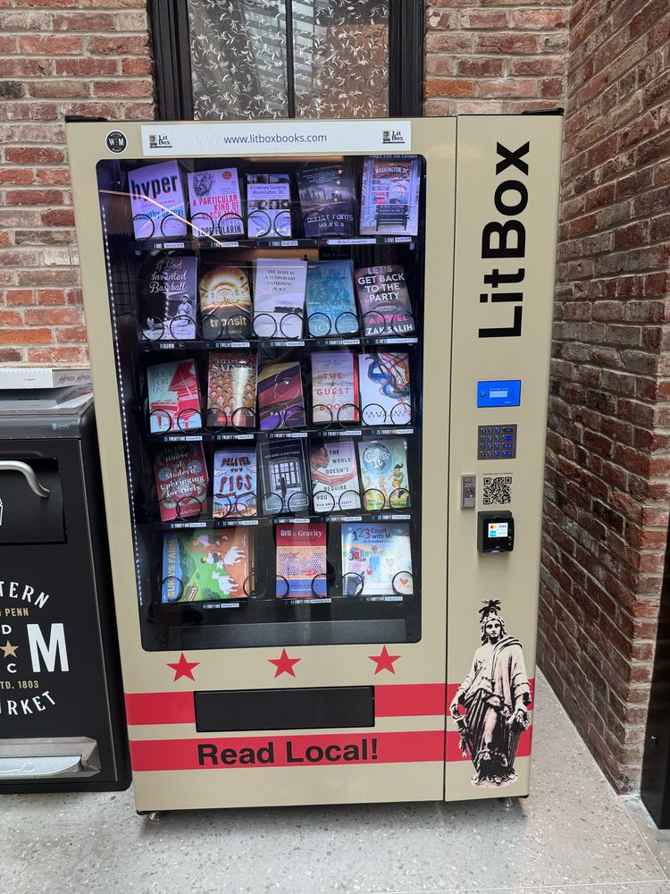 A picture of a vending machine filled with books with a sign saying “Read Local!” Imposed upon the DC flag