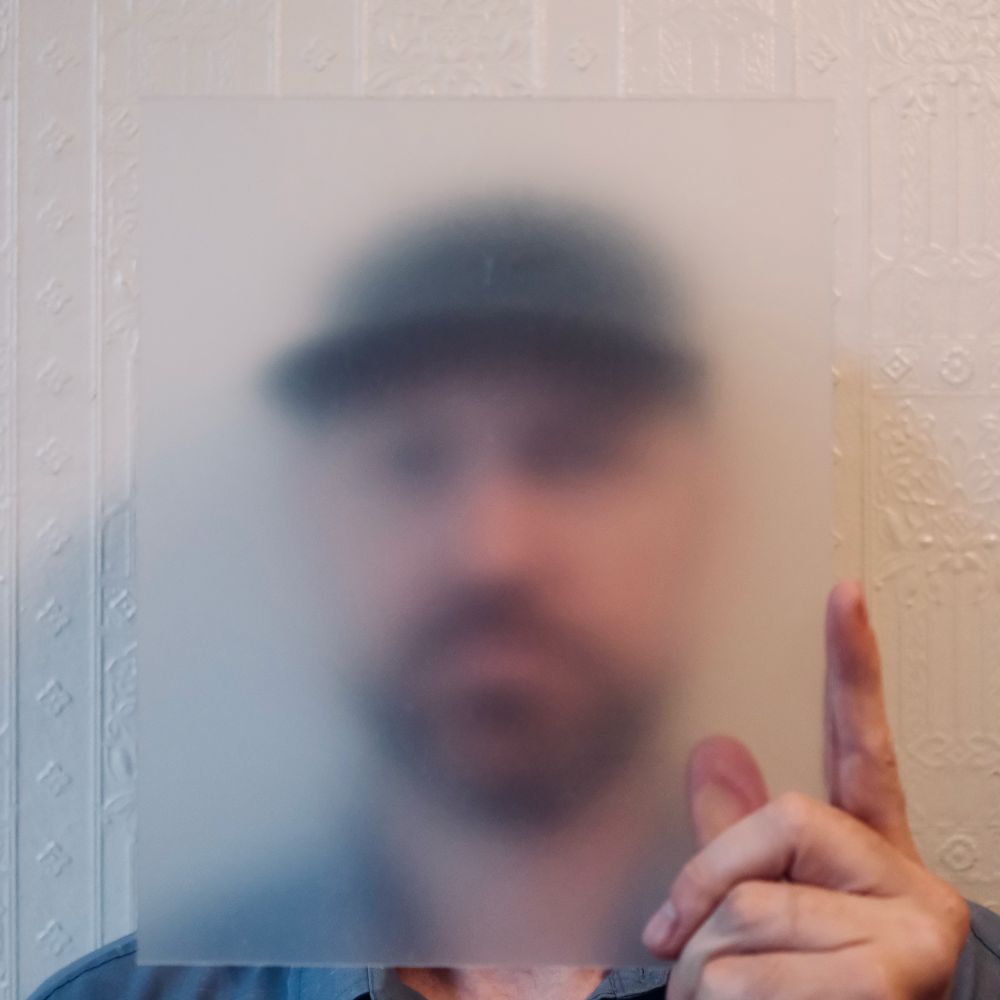 A man holding frosted glass in front of his face, obscuring discernible facial features.