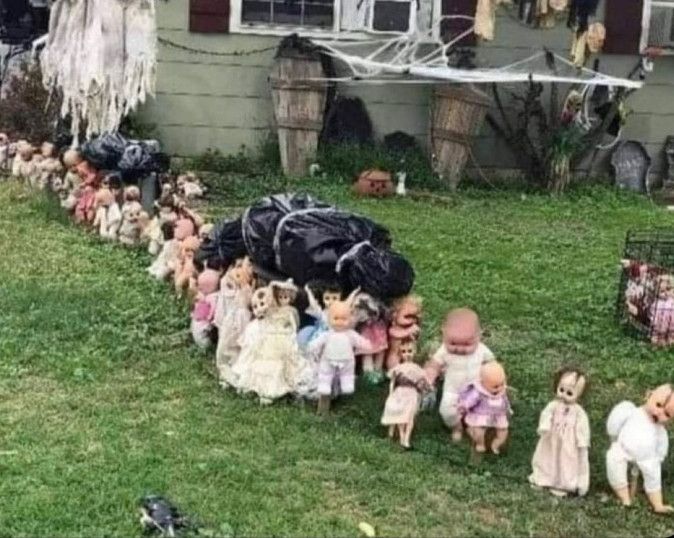 A line of dolls proceeding across a yard, carrying what appear to be two human bodies wrapped in garbage bags. 