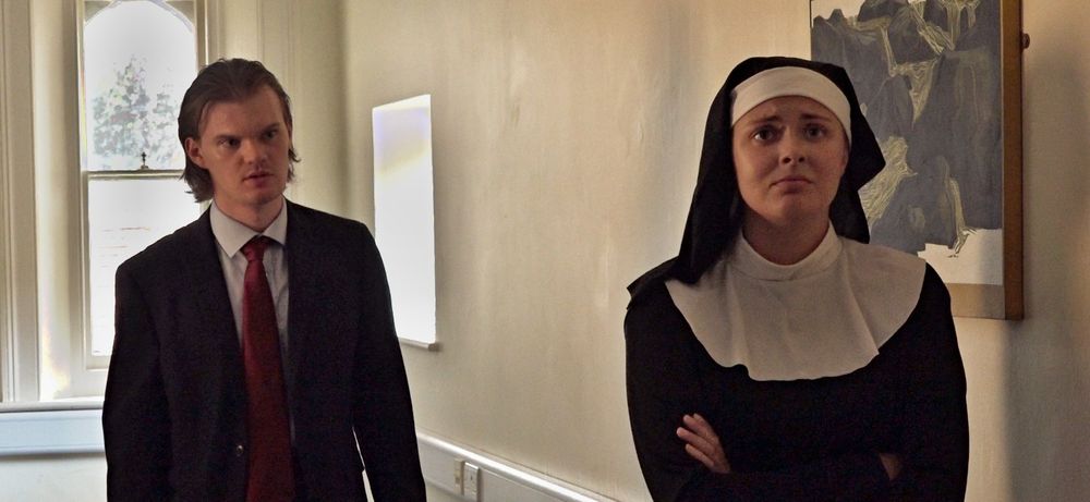Angelo (a man in a suit & red tie) stands behind Isabella (a nun)