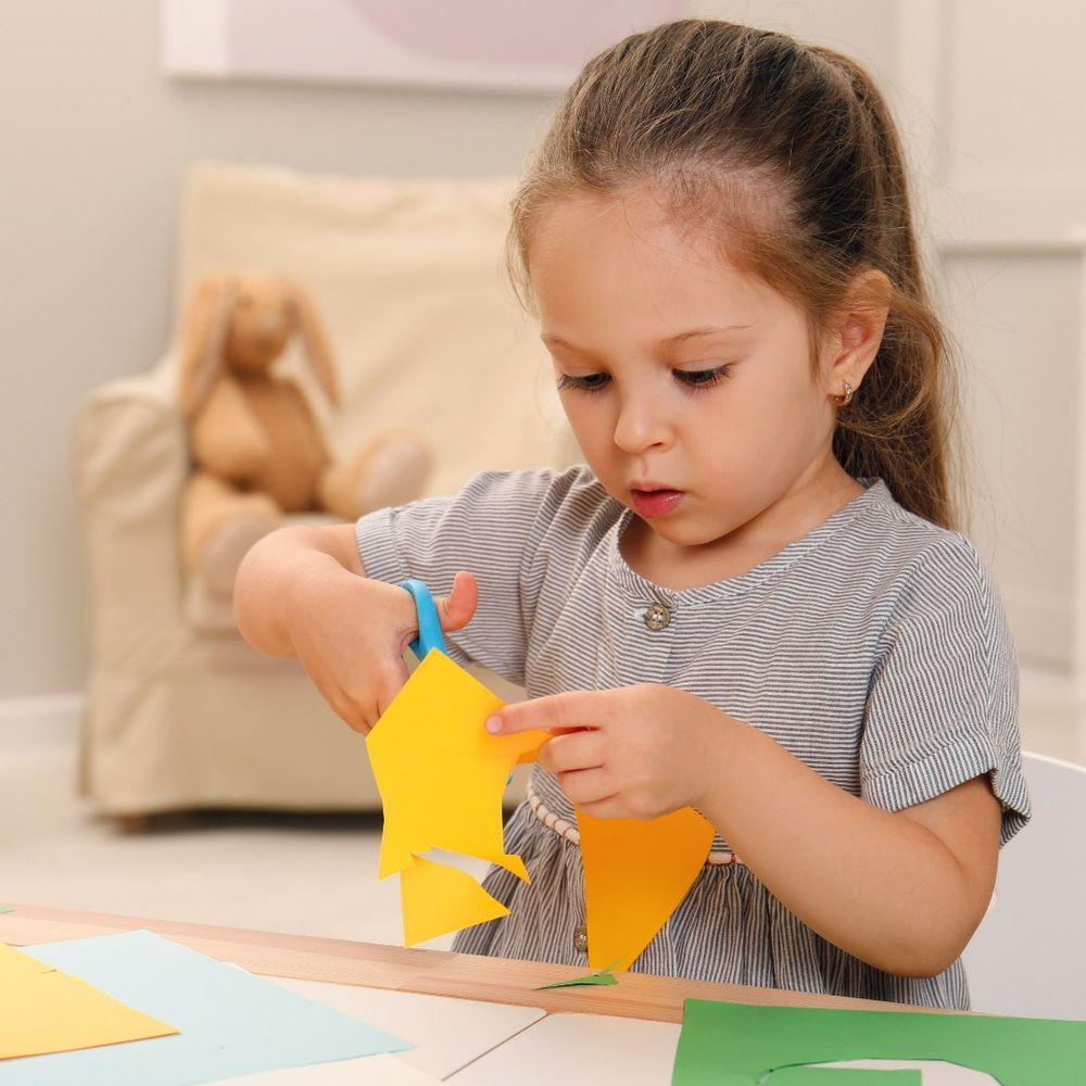 A child is concentrating as she cuts shapes out of colourful paper. 
