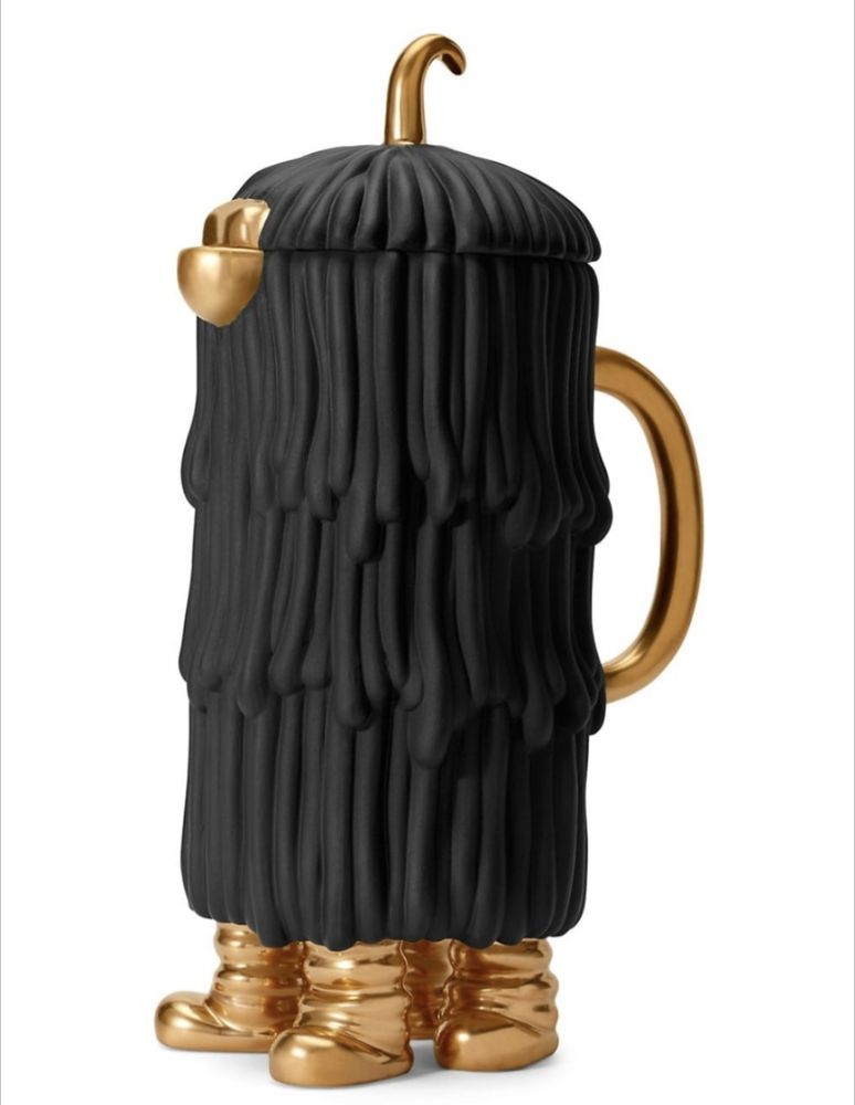 A carafe made to look like a weird creature covered in black, ropey hair, with a small gold beak peaking out and four gold boots propping it up from the bottom. 