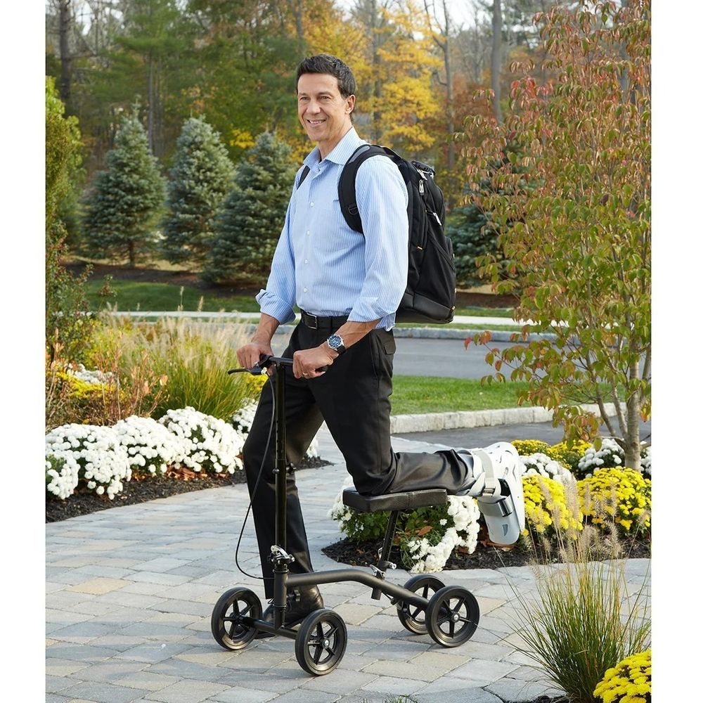 A product photo of a dude in an injury boot using a kneeling scooter