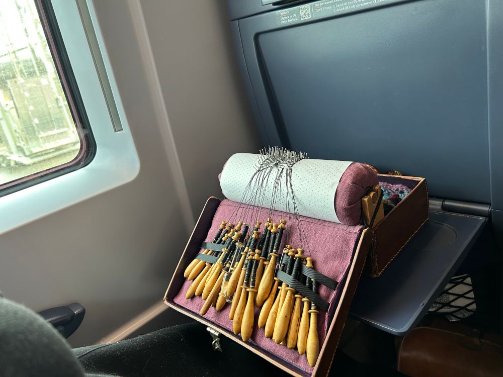 The lacemaking kit on the fold-down table of a train seat.
