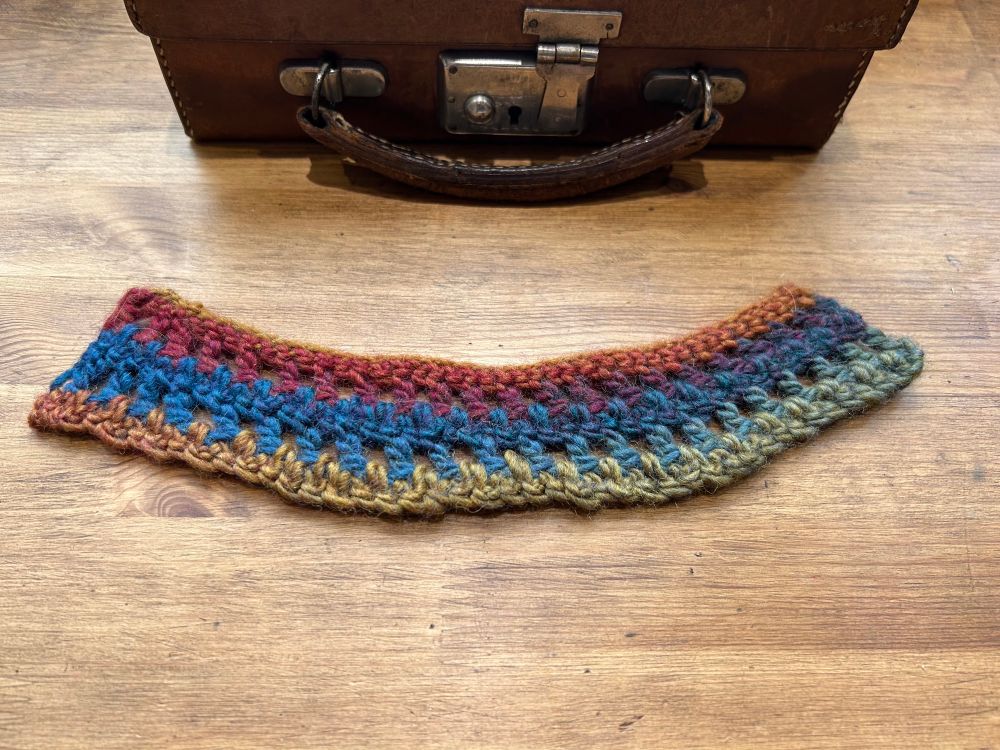 An example of a crocheted bobbin holder. It’s a strip of crochet with two rows of holes in it, big enough to thread one end of a lacemaking bobbin through it.