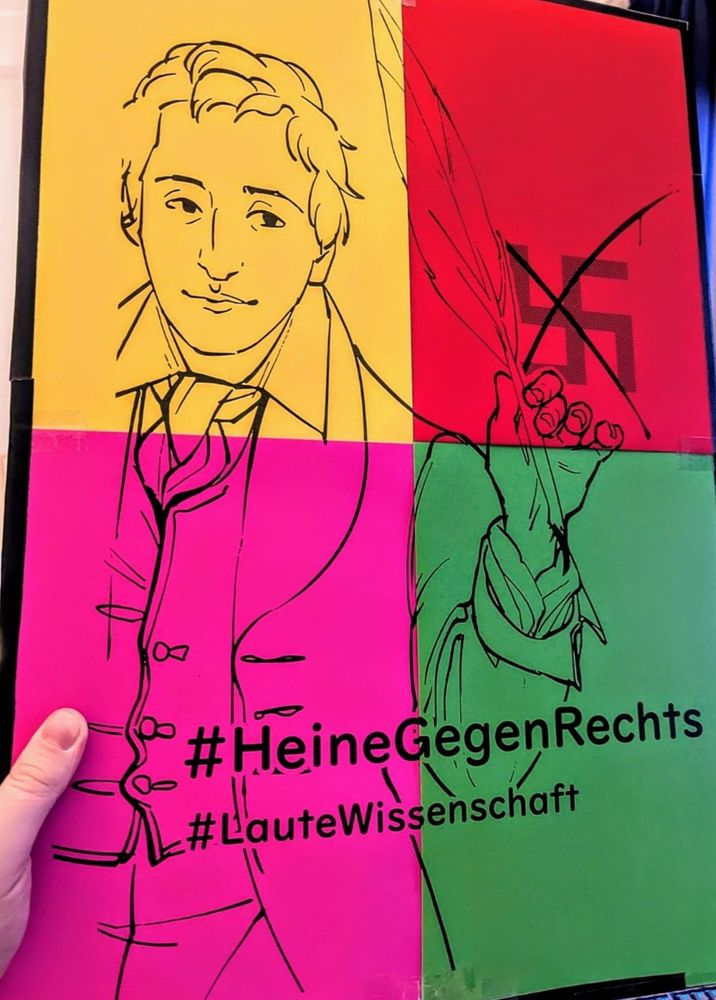 Gebasteltes Demo-Plakat, auf welchem Heine zu sehen ist, der mit einer Schreibfeder ein Hakenkreuz durchstreicht. Statt des üblichen gelben Hintergrunds besteht diese Version aus 4 Blättern mit gelber, roter, pinker und grüner Farbe.