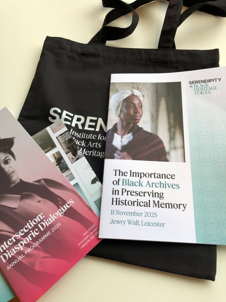 On a table a black tote bag and printed conference materials. The main one has a photo of a black woman in shawl and head covering with title The importance of black archives in preserving historical memory. 
