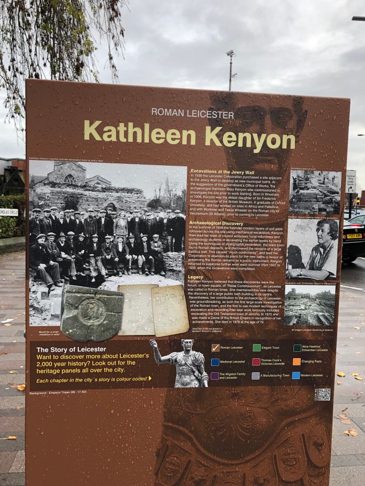 Photo of large plaque on a street about Kathleen Kenyon. Black and white photos of the woman and a large team of archaeologists and the site in the 1930s. 