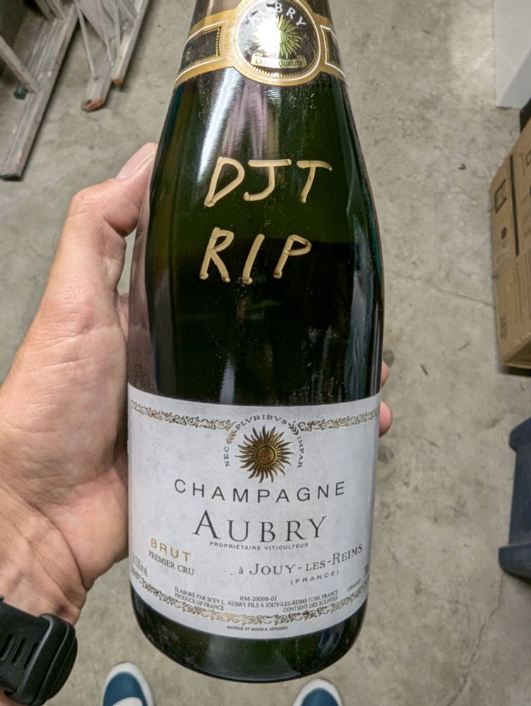 A bottle of Champagne Aubry brut with "DJT RIP" written in marker