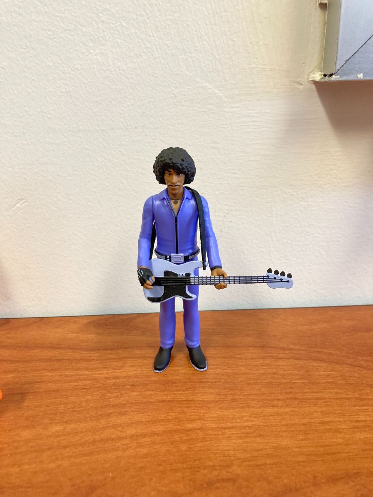 Phil Lynott action figure. Phil is wearing a purple jumpsuit and is holding a bass guitar. 