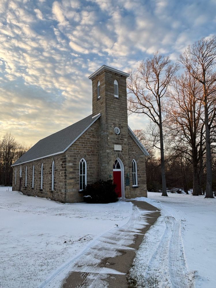 Small stone country church with a red door with evening light and clouds as a backdrop 