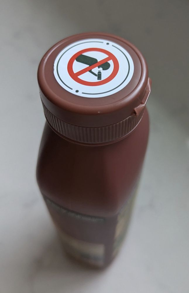 Photo of a bottle of shampoo with a sticker on the lid. It depicts a simple icon of someone about to pour the liquid in their mouth with the universal 'stop' icon over it.