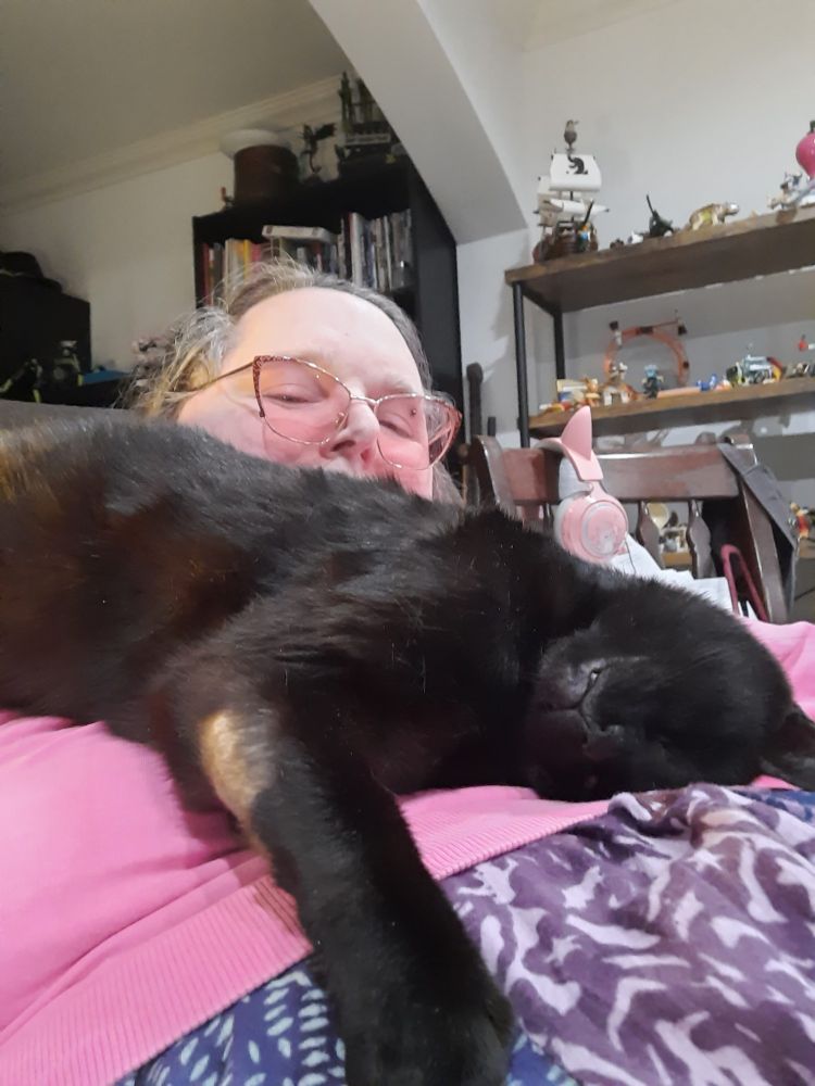 Lily in a pink sweater, mostly hidden behind a black cat draped all over her and looking happy.