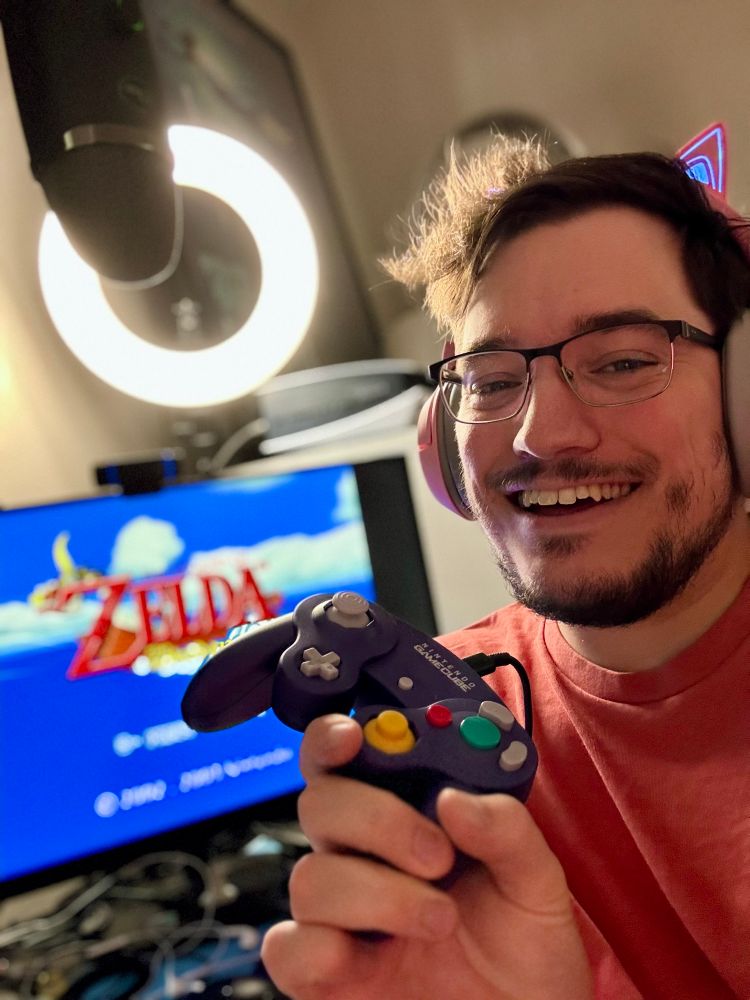 Simon holding a Game Cube controller with a screen showing The Legend of Zelda: Wind Waker in the background 