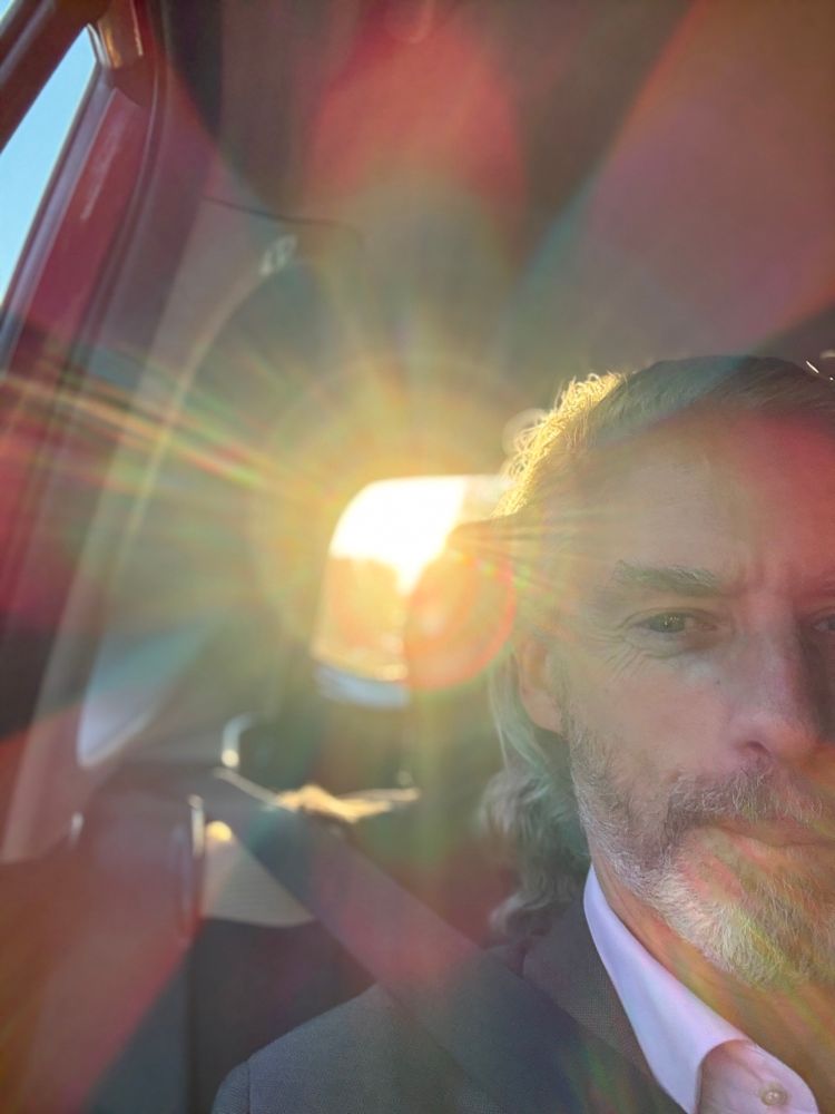 Selfie of white man in rear seat of car, with massive lens flare from the sun in the rear window. 