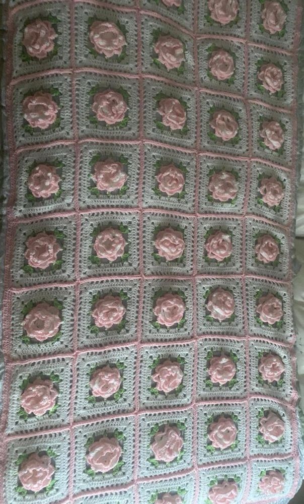 A grannysquare blanket with roses laying on a bed, photographed from above