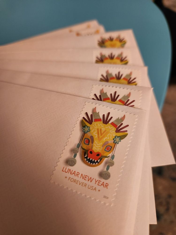 A photo of a stack of white envelopes. The focus is on a Lunar New Year stamp for the year of the dragon.
