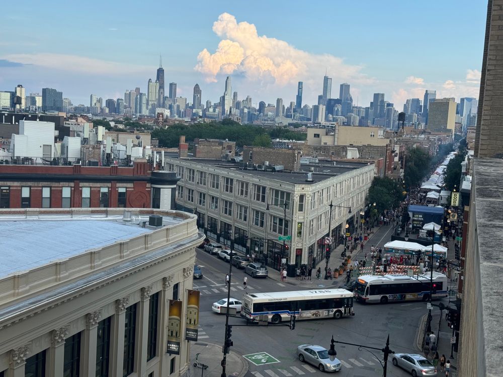 Southeast view of Milwaukee Ave and downtown Chicago from on top of a building showing CTA buses, festival tents, and many skyscrapers in the distance.
