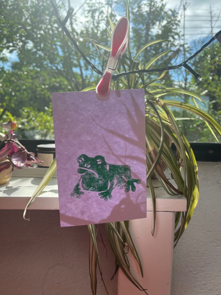A white piece of paper with a green linocut print of a toad, hung to dry with a clothespin