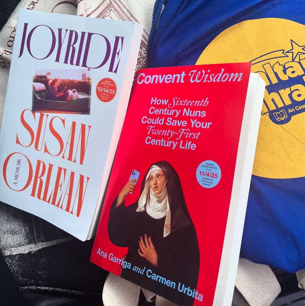 Advance reader copies of Joyride: A Memoir by Susan Orlean and Convent Wisdom: How Sixteenth Century Nuns Could Save Your Twenty-First Century Life by Ana Garriga and Carmen Urbita, on top of two tote bags on a very sandy car seat 