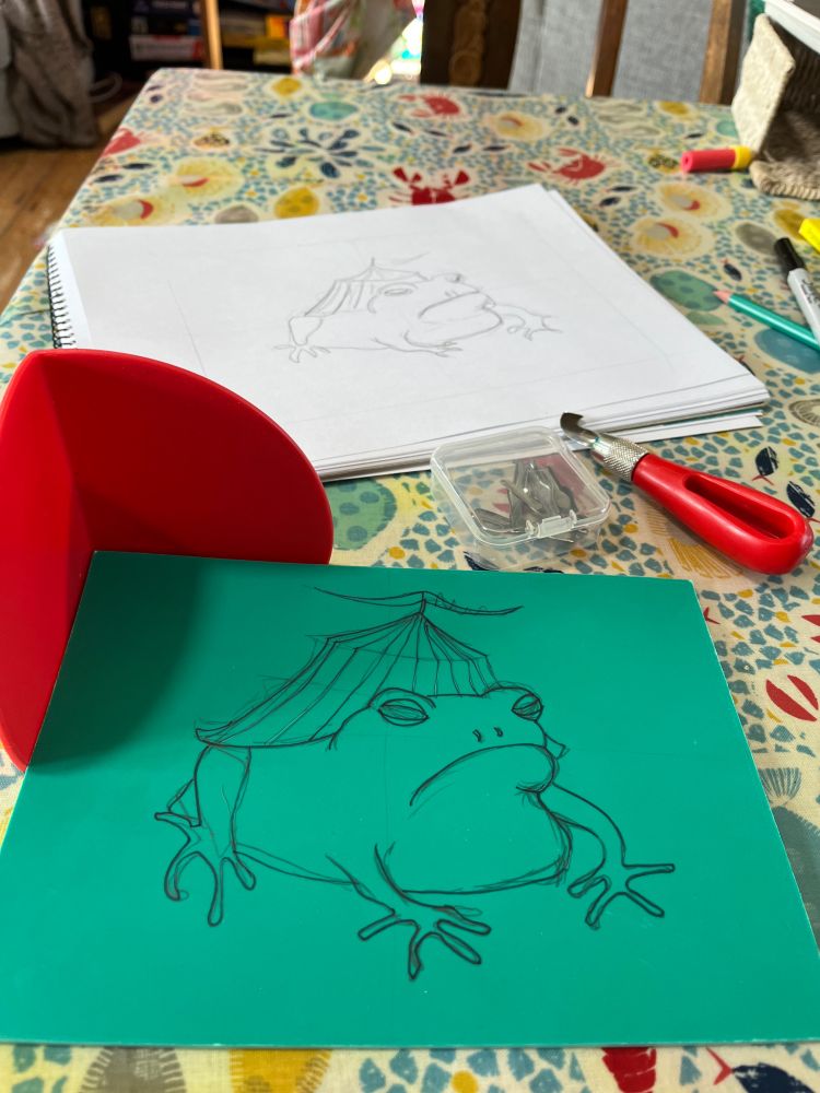 A linoleum print block with a line drawing of a circus tent on a toad’s back