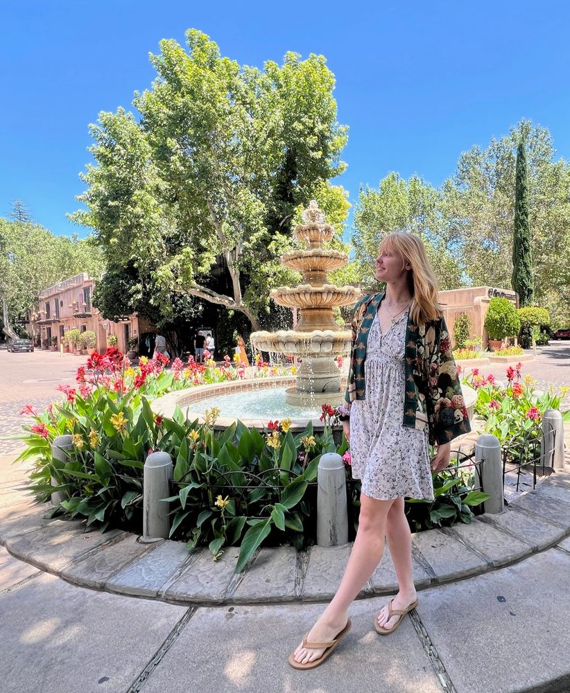Seri standing in flip flops, a dress and kimono near a fountain in Sedona, Arizona with her hair down 