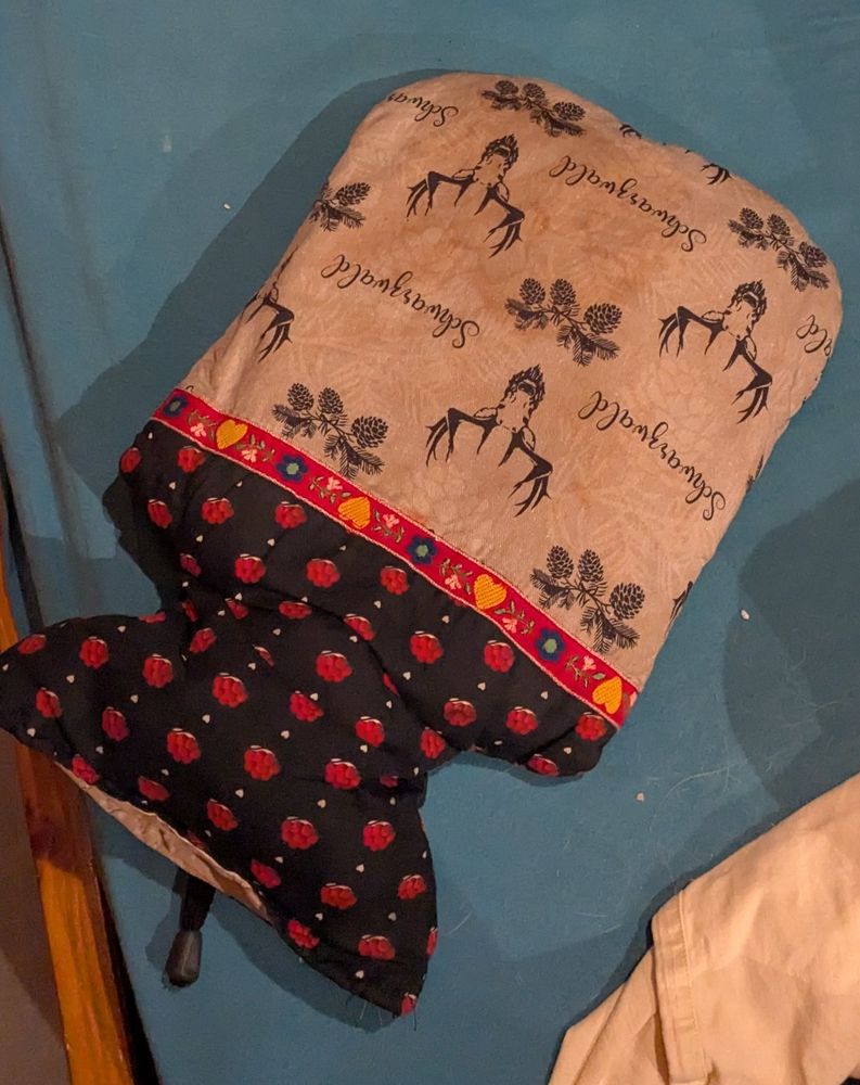 Foto Wärmflasche.
Wärmflaschenhülle:
oberer Teil der Flasche kleine rote Bommelhüte auf schwarz.
Untere Teil Elche skizziert auf hellgrauem Stoff.
Aufschriften "Schwarzwald"

weil von Flaschenöffung aus fotografiert, sehen die Elche Bisschen aus wie Mittelfingerhände