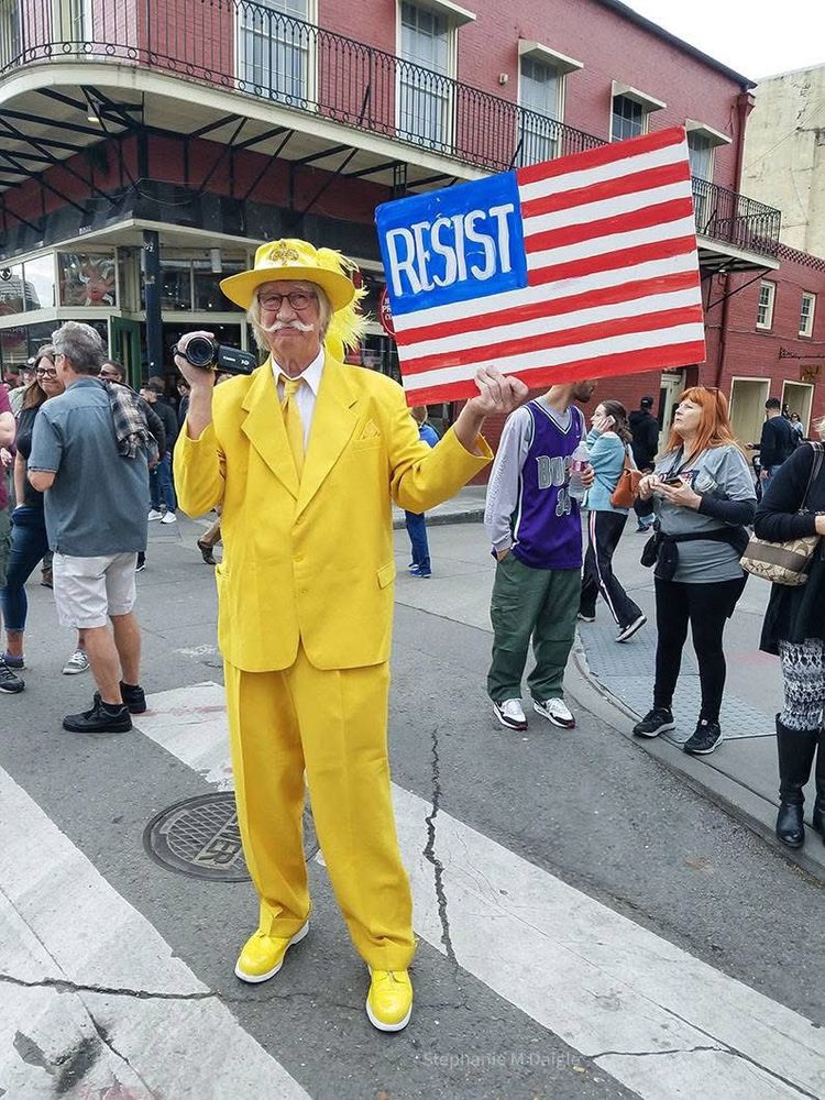 Man in bright yellow in the French Quarter holding a sign depicting RESIST 