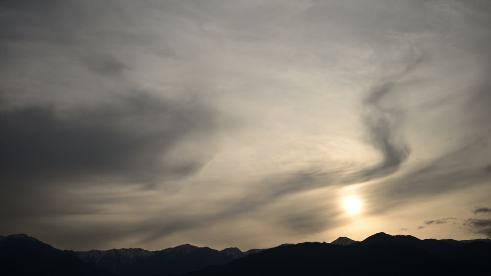 太陽が写真下の山々へ沈み始める、まだ完全に出ているときに撮影
太陽は雲に少し遮られていて、雲がうねうねしたかたちで浮かんでいる