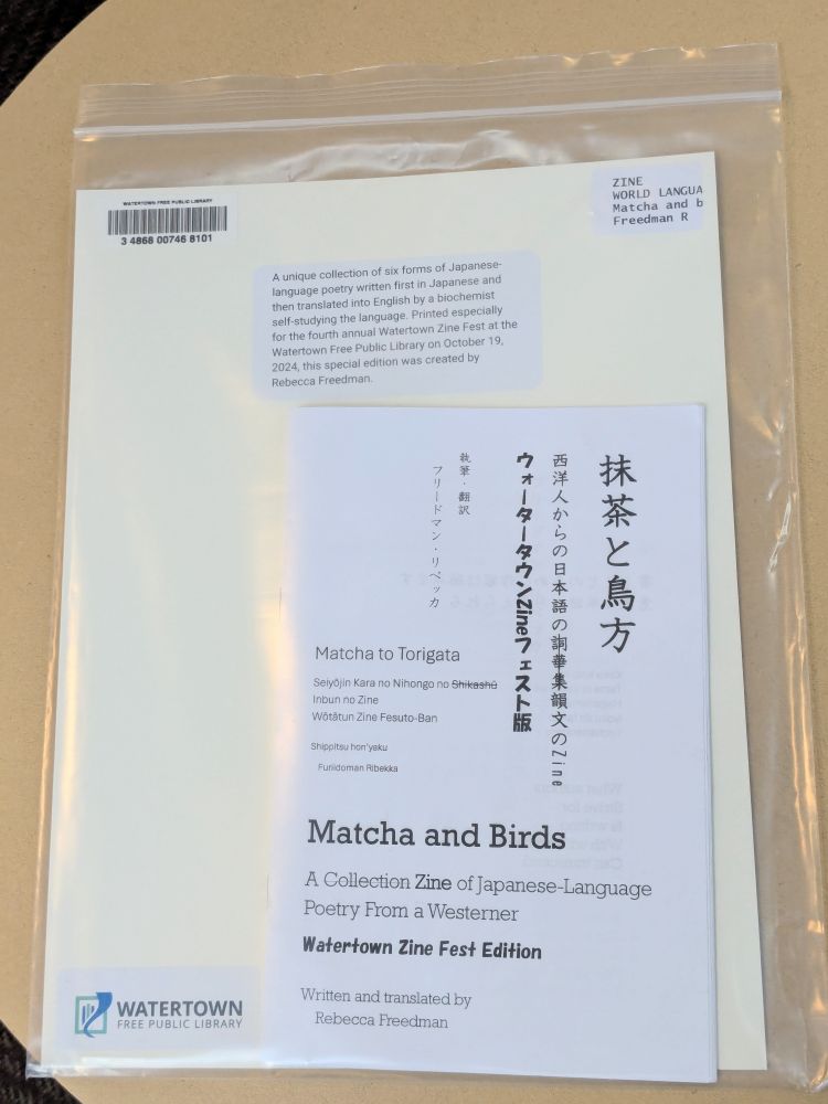 A photo of a copy of the zine edition of Matcha and Birds/抹茶と鳥方, inside a plastic ziplock bag with Watertown Free Public Library's cataloging cardboard sheet.