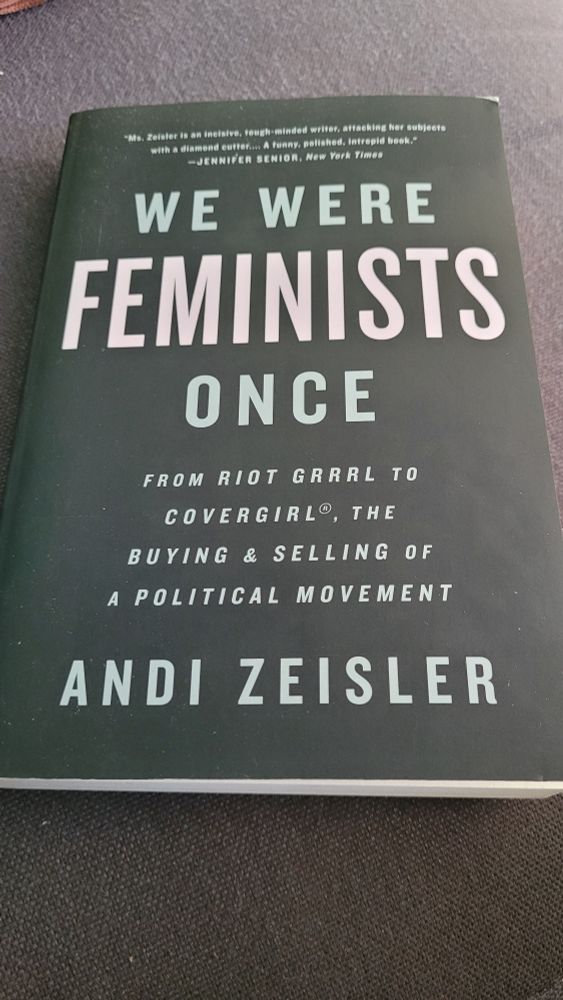Op een grijze, stoffen ondergrond ligt het paperback boek "We Were Feminists Once" van Andi Zeisler. De kaft van het boek is zwart met lichtgrijze tekst, op het woord feminists na, dat is lichtroze. Tekst op de kaft: "Ms. Zeisler is an incisive, tough-minded writer, attacking her subjects with a diamond cutter... A funny, polished, intrepid book." - JENNIFER SENIOR, New York Times 
WE WERE FEMINISTS ONCE
FROM RIOT GRRRL TO COVERGIRL, THE BUYING & SELLING OF A POLITICAL MOVEMENT
ANDI ZEISLER" 
