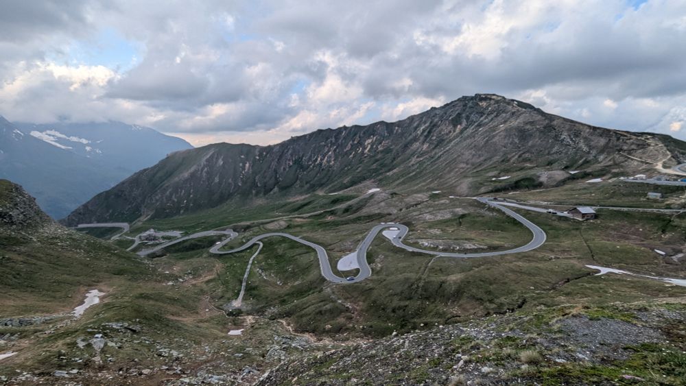 Blick vom Fuscher Törl runter auf die Großglockner Hochalpenstraße. Die graue Straße schlängelt sich auf den braun/grünen Hängen hoch.