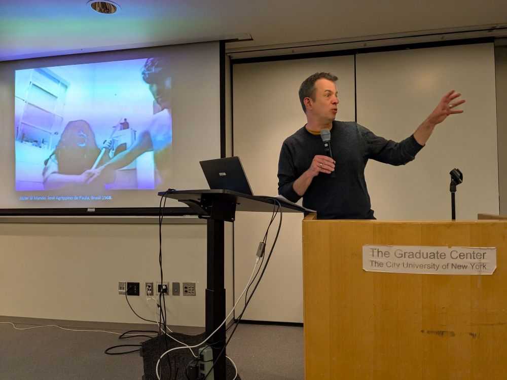 Jens Andermann giving a talk at The Graduate Center. A clip of a film on the screen.