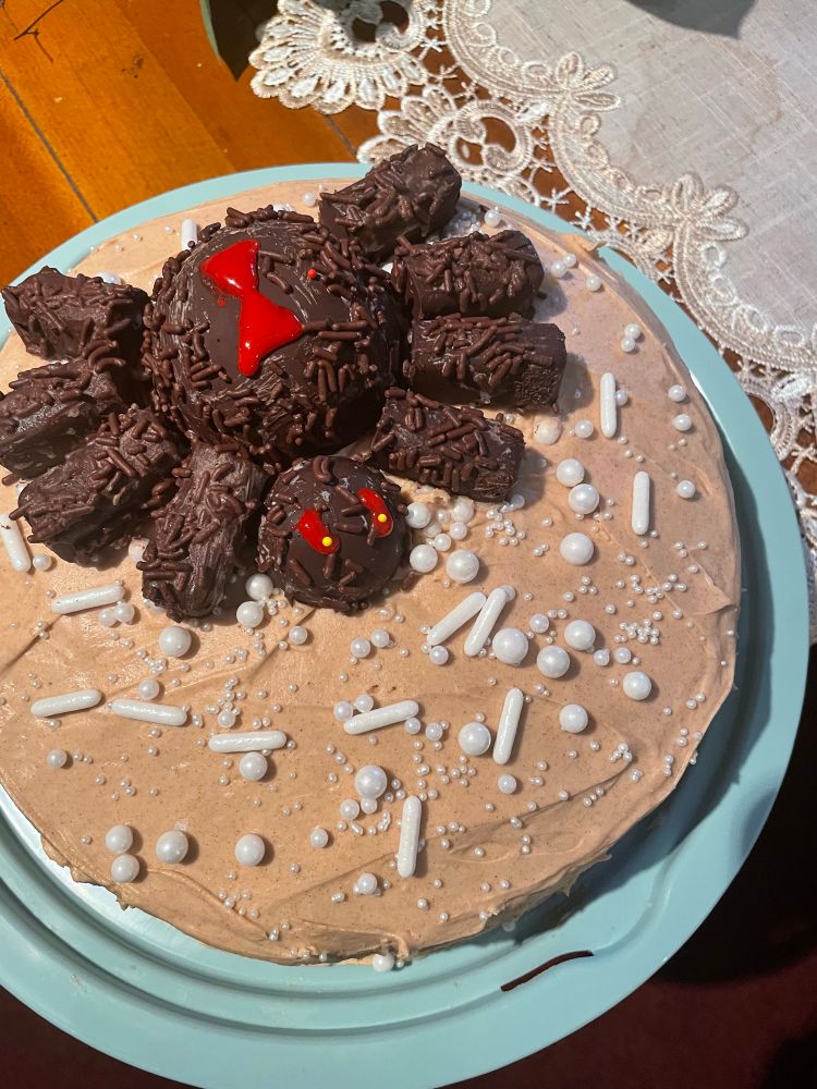 Pumpkin spice cake with cinnamon cream cheese frosting. On top is a chocolate spider surrounded by white spider eggs, which are round and oblong pearl sprinkles. It’s a cake for my sister’s birthday and my first attempt at decorating. 
