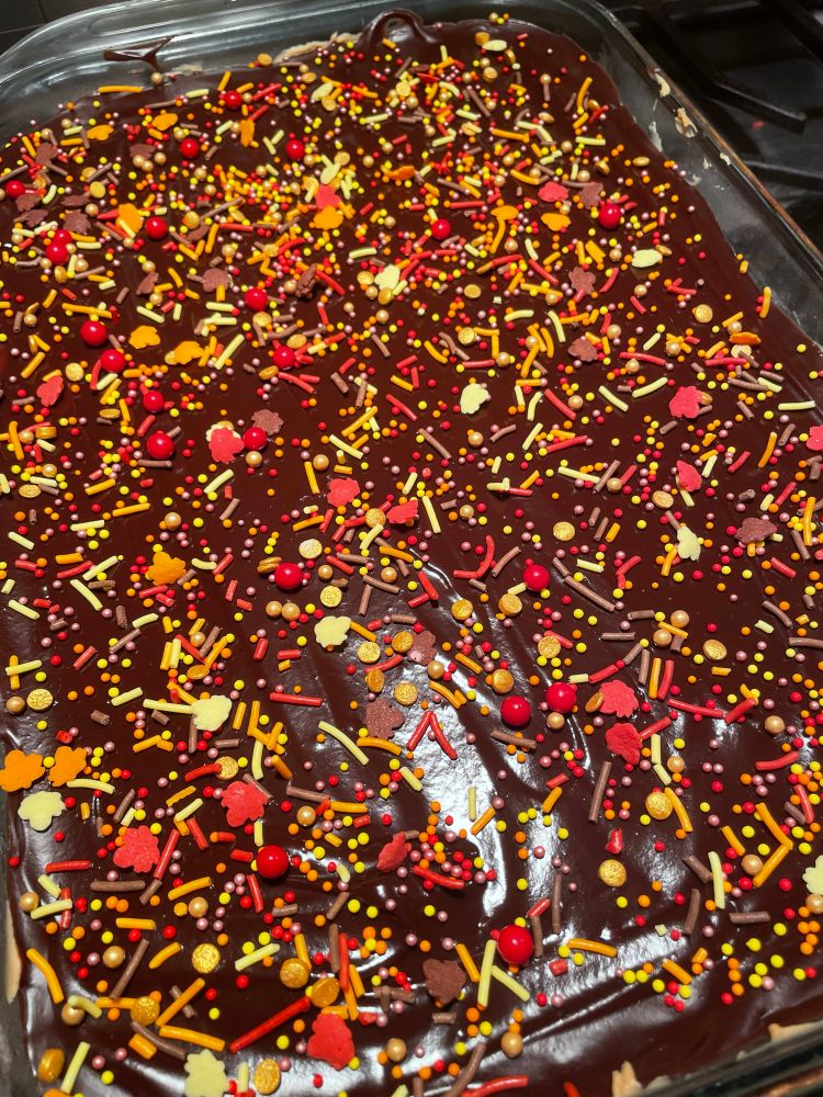 The top layer of a peanut butter ‘pie’ made of chocolate ganache.  It is covered in multicolored fall leaf sprinkles. 