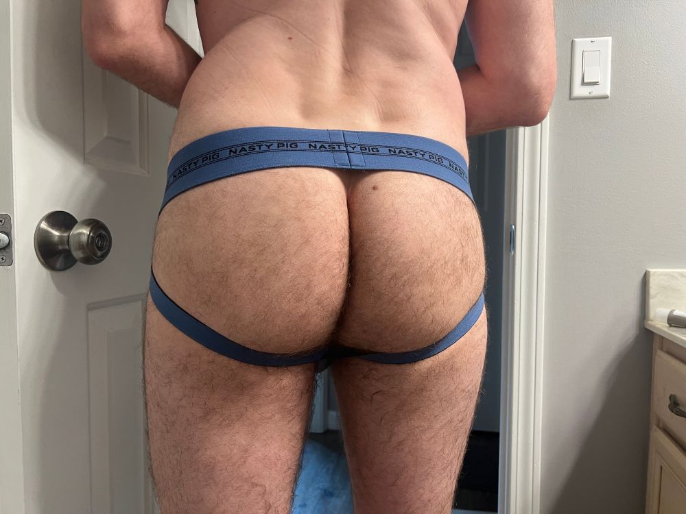 Picture taken from behind of a bare furry ass in a blue Nastypig jockstrap