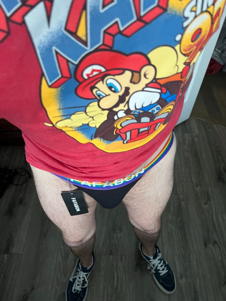 Man in a Fafabon jockstrap with rainbow band, Mariokart tshirt and vans tennis shoes.