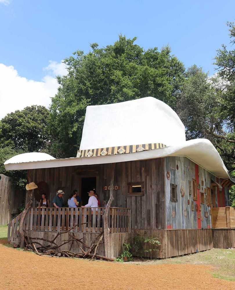 A photo of a simple wood plank house with a giant Stetson hat for a roof.  The roof hat is white so you know the house is not a cattle rustler or poker cheat.