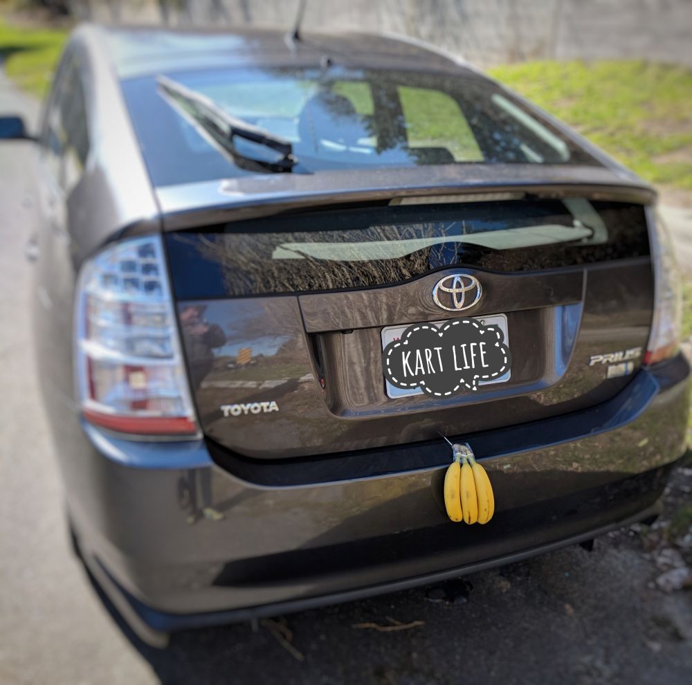 Toyota Prius with three bananas hanging from the rear bumper on a sunny day 