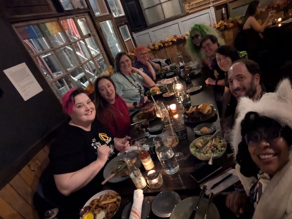 Nine members of TTN smiling for a selfie at a restaurant table. 