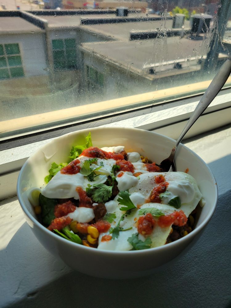Picture of eggs with a salsa and yogurt drizzle over greens and a sweet potato hash topped with cilantro in a white bowl