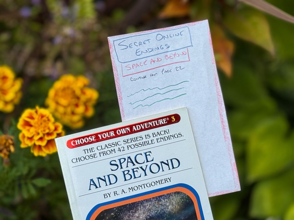 An open book titled "Space and Beyond" from the "Choose Your Own Adventure" series is displayed, alongside a handwritten note labeled "Secret Online Endings" that references content related to the book. The background features yellow marigold flowers.