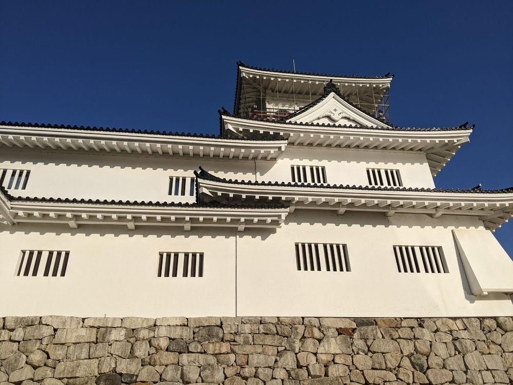 Vertical slotted windows on the white walls above stone of Toyama Castle from one side