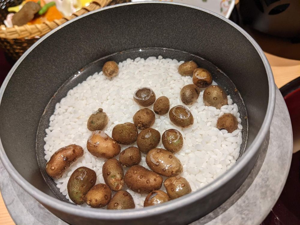 A small pot with rice (uncooked) and teeny potato looking things